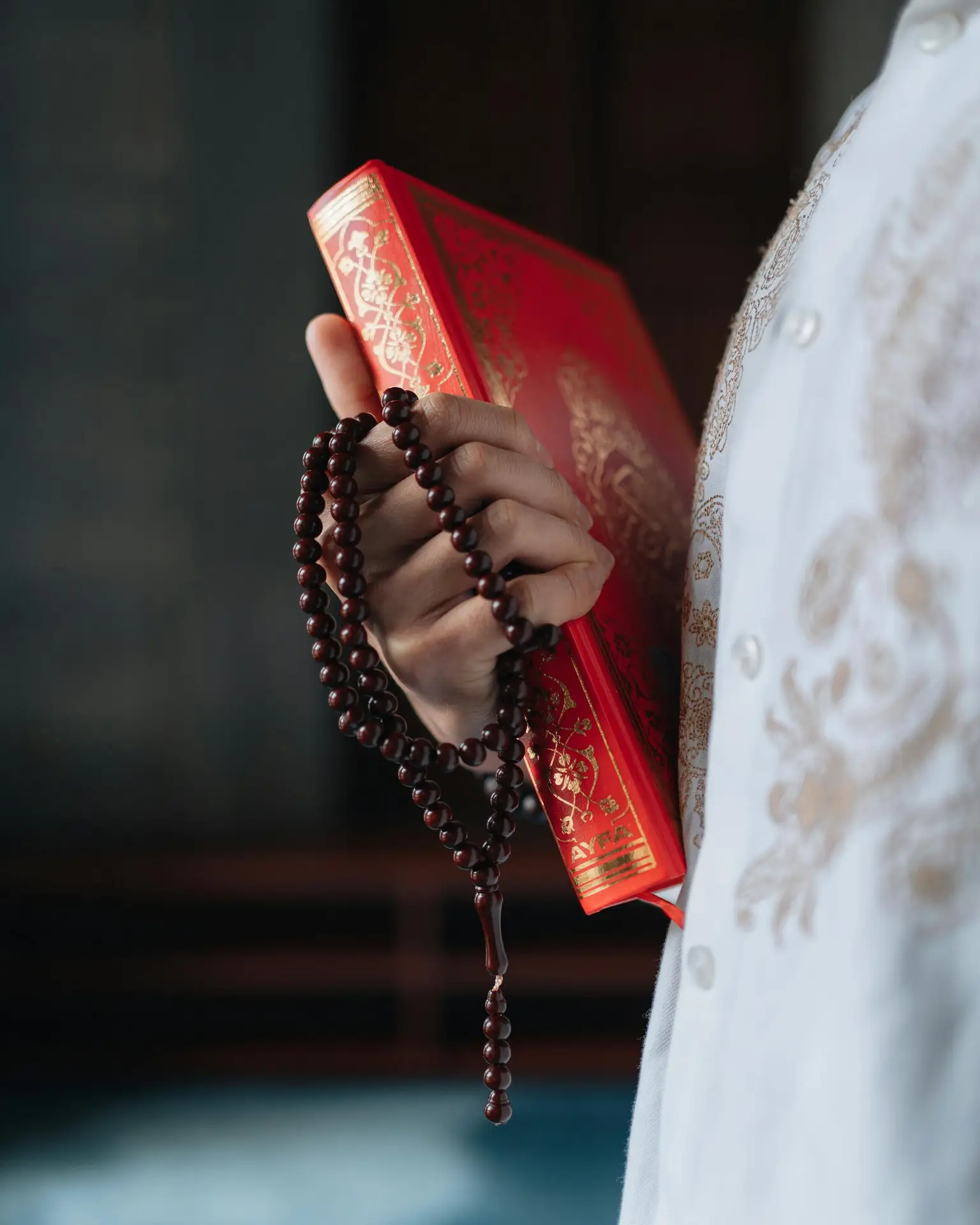 A close-up shot of a hand holding a Quran with prayer beads, symbolizing Islamic faith and spirituality.